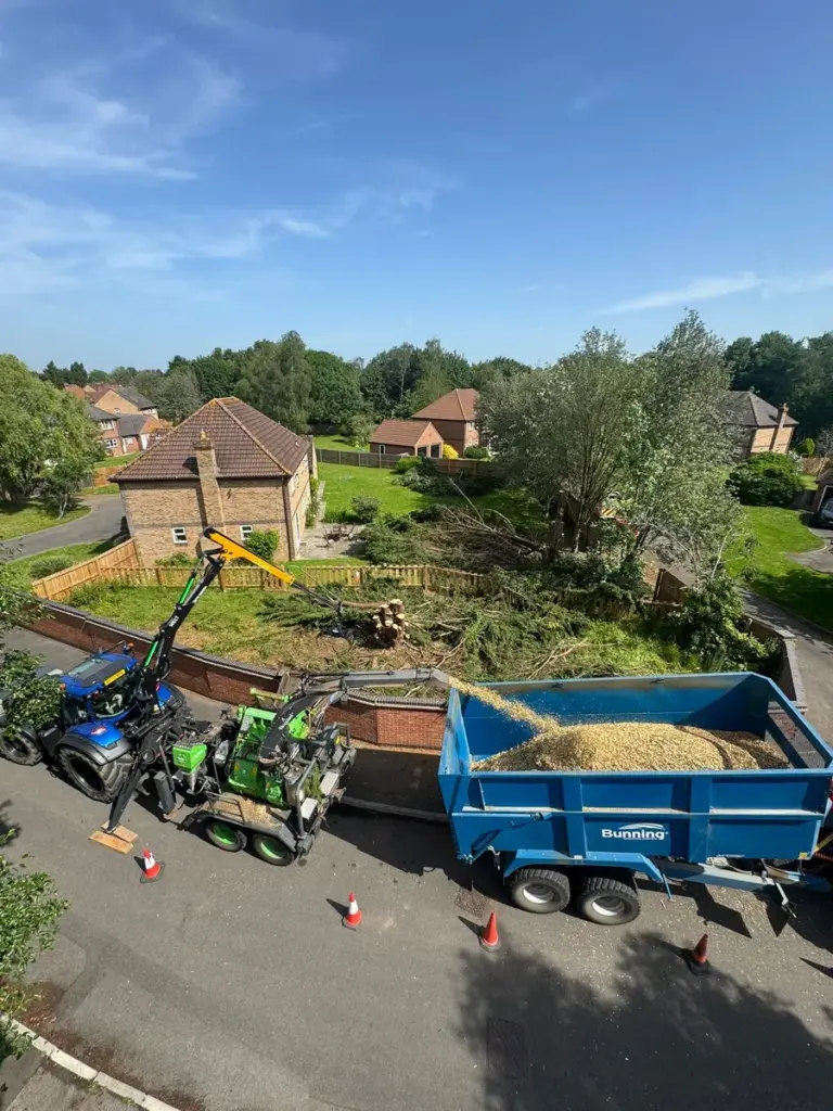 A large tractor and wood chipper spraying woodchip into a truck bed