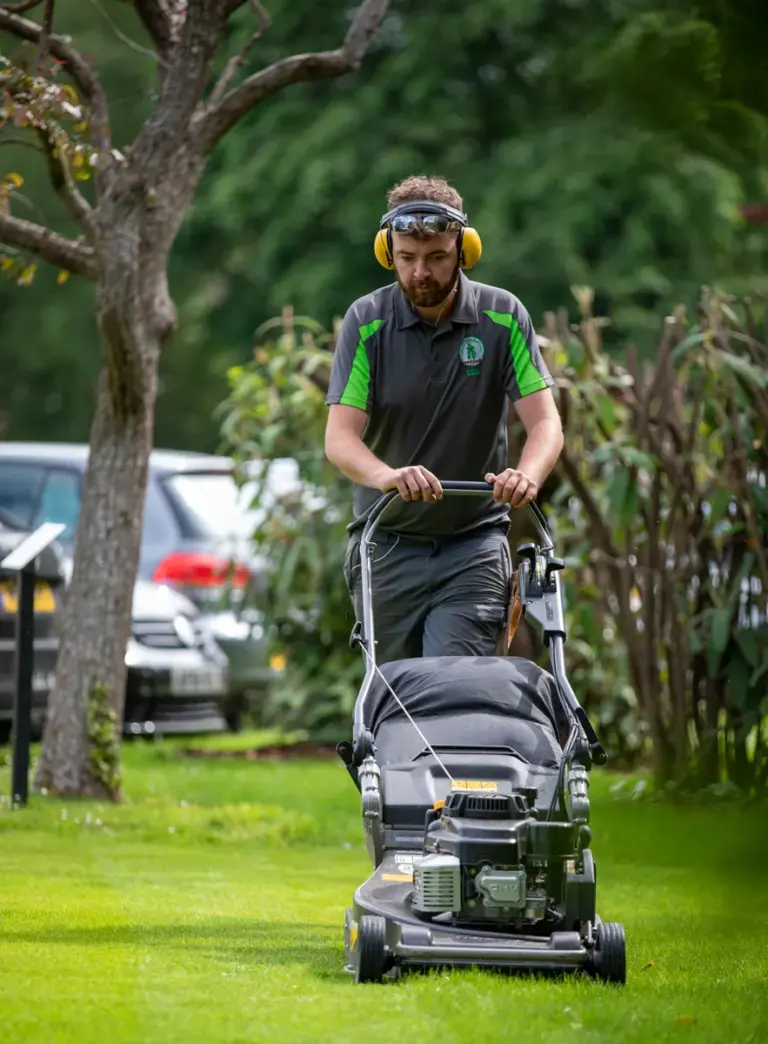 A silver tree services staff member uses a lawn mower with sunglasses on.
